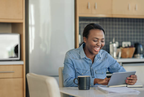 istock Laughing African American woman using a tablet in her kitchen 2185771367