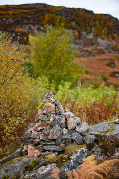 This is a photograph of a rock cairn stacked on the hillside of a mountain in Cairngorms National Park in the Scotland Highlands with autumn leaf foliage on an overcast October day.