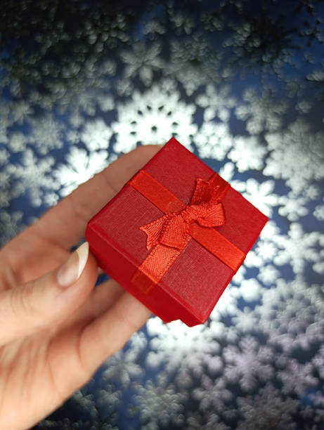 istock Red gift box in a female hand on a blue background with snowflakes 2185780566