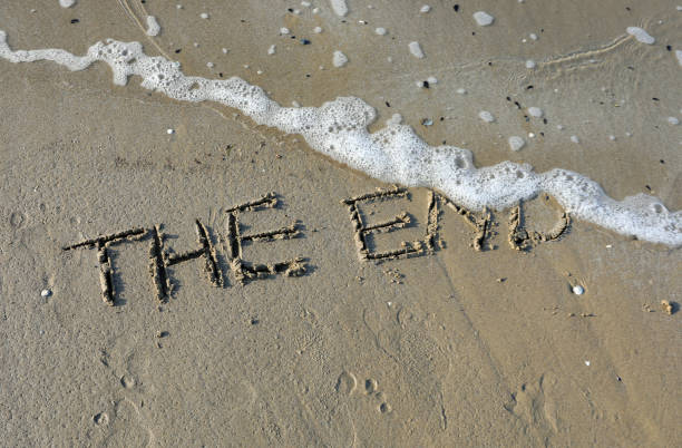 words the end written on a sandy beach with a wave about to erase them