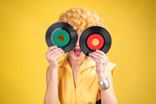 A woman dressed as it it were the 1970s holding two 45 records over her eyes.