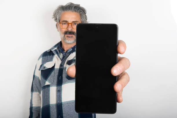 man showing mobile phone screen holding and looking at camera isolated in white background.