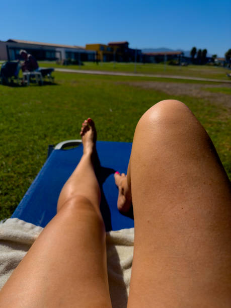 A person is relaxing on a lounge chair in a green space, soaking up the sun under a clear blue sky. The scene captures the essence of a leisurely afternoon outdoors.