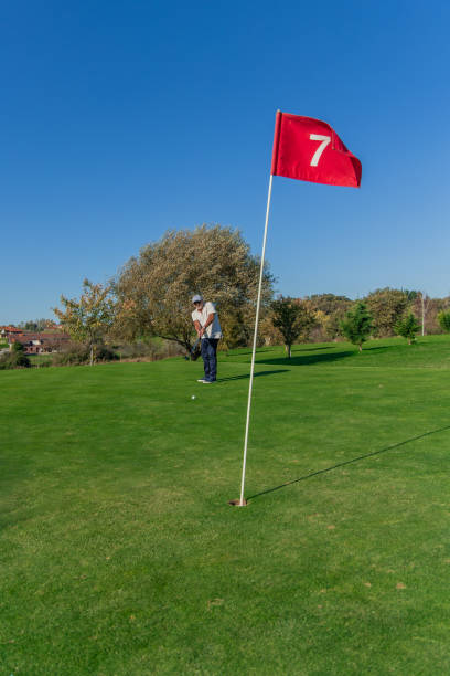 istock vertical golf ball heading toward hole on green with senior golfer practicing in background 2185794859