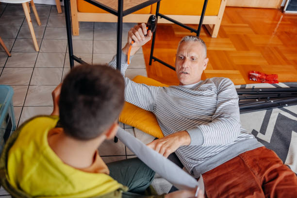 istock Father and son moving in new home and assembling shelf together while looking at construction plan 2185797556