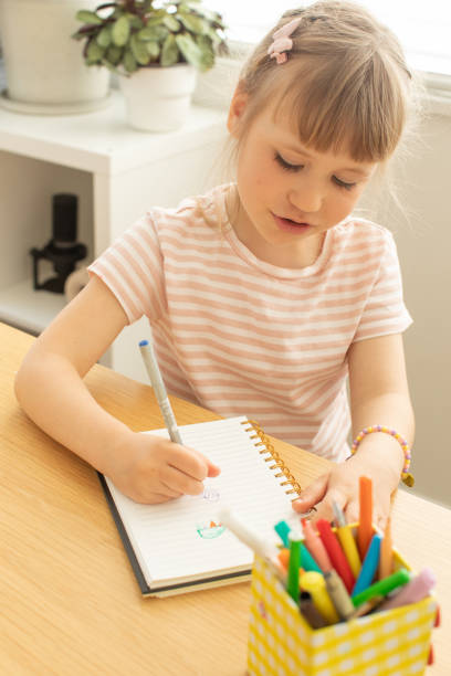 istock Cute little girl draws picture on notepad page at table 2185800158