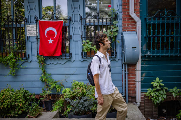 A man with a backpack strolls by a building with a Turkish flag, taking in the vibrant street scene in this lively urban snapshot, emphasizing national pride.