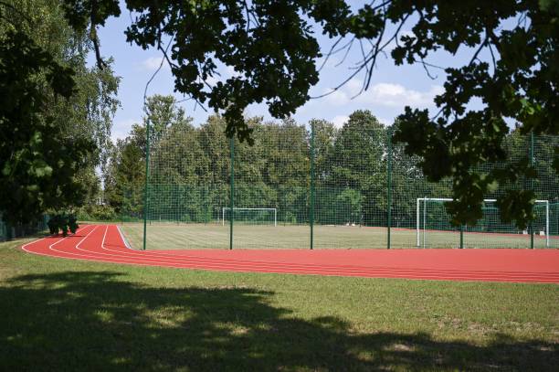 Bright red running track with white lane markings surrounded by lush green trees