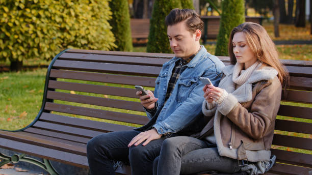 istock Caucasian couple two young people partners sit on bench use phone cell gadgets scroll internet web pages check social networks show images each other spend time in city park suffer of mobile addiction 2185808885
