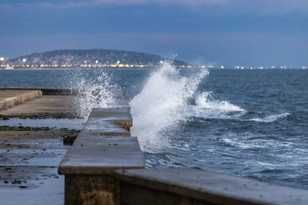 Breaking waves on coastline.\nWindy weather conditions.