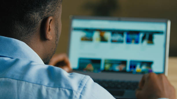 istock Backside unknown man african american businessman web designer employee sit at home office searching films TV series on internet website e-service looking at computer laptop screen over shoulder view 2185812240