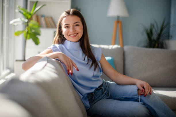 istock Smiling young lady comfortably seated on a cozy couch. 2185830599