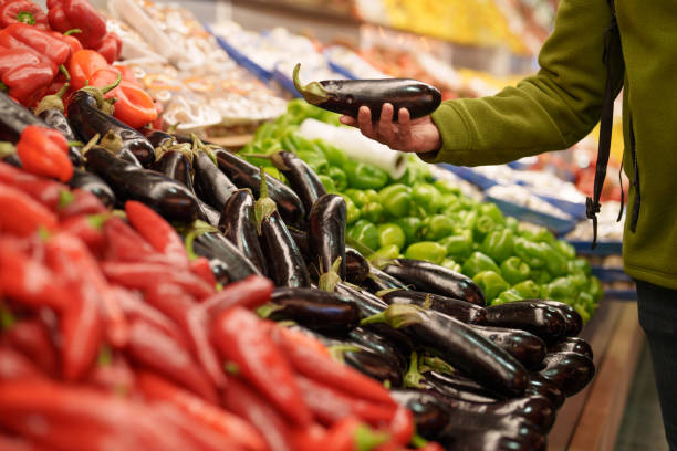 Close-up of a man's hands picking eggplants at the produce section.
