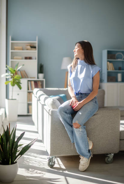 istock Woman in blue top sitting on couch enjoying sunlight 2185832349