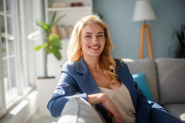 istock Woman smiling on a sunlit couch in blue blazer suit 2185833209