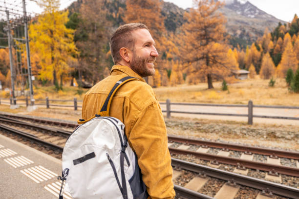 A cheerful man with a backpack stands on a train platform surrounded by stunning fall foliage, embodying the spirit of adventure and seasonal travel.