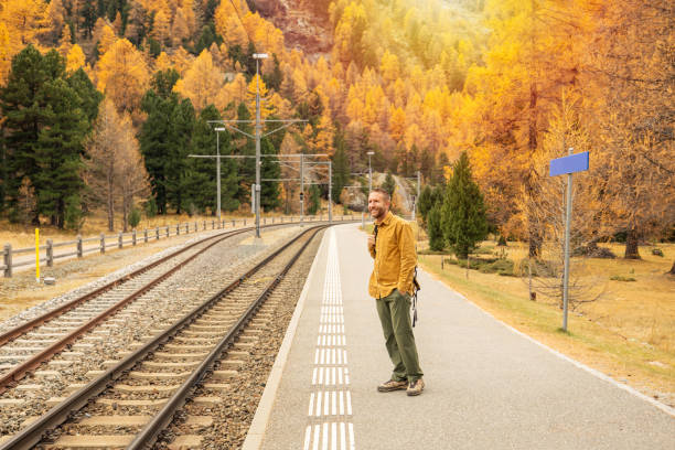 A cheerful man with a backpack stands on a train platform surrounded by stunning fall foliage, embodying the spirit of adventure and seasonal travel.