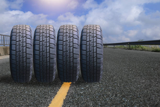 four tires arranged in front of a board on an asphalt road It conveys the readiness of traveling or keeping the car safe at all times.