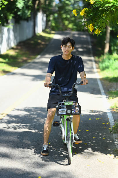 istock Active man riding a green bicycle on tree lined road on a sunny day. Outdoor activities concept 2185859424