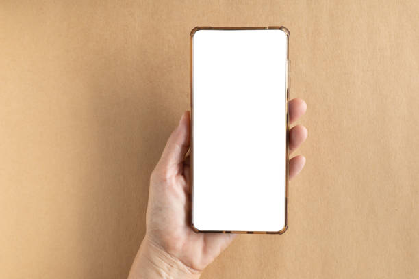 istock Hand-holding smartphone shows a white screen display on brown background. Top view, flat lay with copy space. Concept for business online, blogger, and advertising. 2185862264