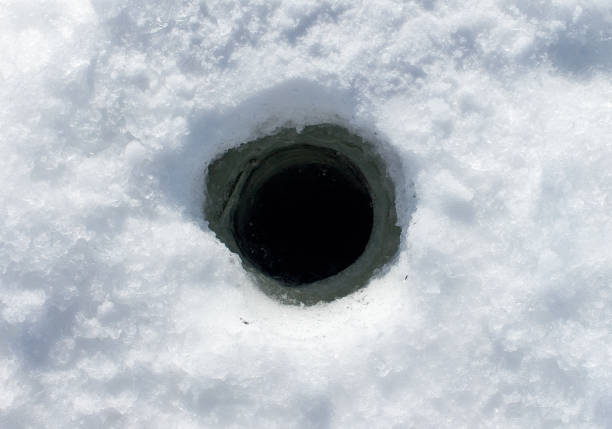 High angle view of a fisherman pulling a net out of an ice fishing hole on a frozen lake, with footprints in the snow and a fish lying nearby