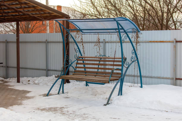 A blue bench with a blue canopy sits in a snow covered yard. The bench is empty and the canopy is closed