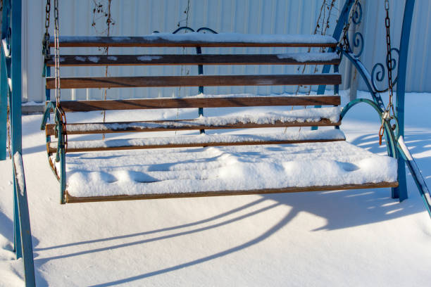 A wooden bench with a chain hanging from it is covered in snow. The bench is empty and the snow is covering it