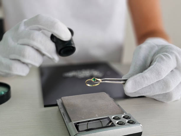 A jeweler examines a gold ring with a green stone using a magnifying glass