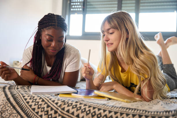 Two female students studying together on a bed, exchanging ideas