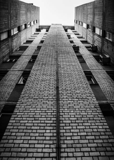 Black and white perspective view of a tall brick building looking up towards the sky, showcasing architectural symmetry and urban design.