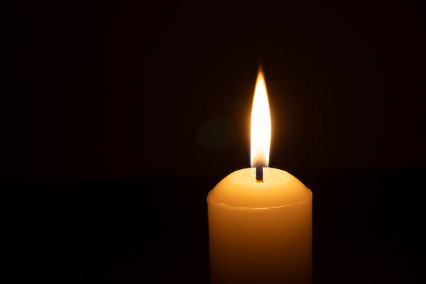 istock A single burning candle flame or light glowing on a big white candle isolated on black or dark background on table in church for Christmas, funeral or memorial service 2185871839