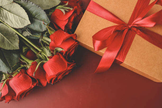 istock A brown gift box tied with a white ribbon rests on a red surface alongside fresh red roses. A romantic and elegant composition perfect for occasions like Valentine's Day, anniversaries, or gifting 2185877221