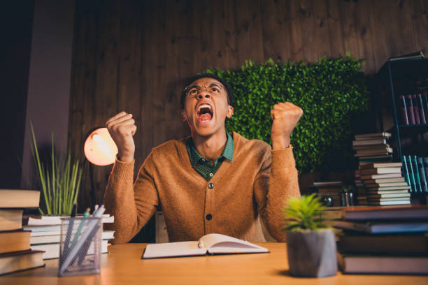 istock Young student celebrating success while studying at home on a relaxing evening indoors, surrounded by books and notebooks. 2185878000