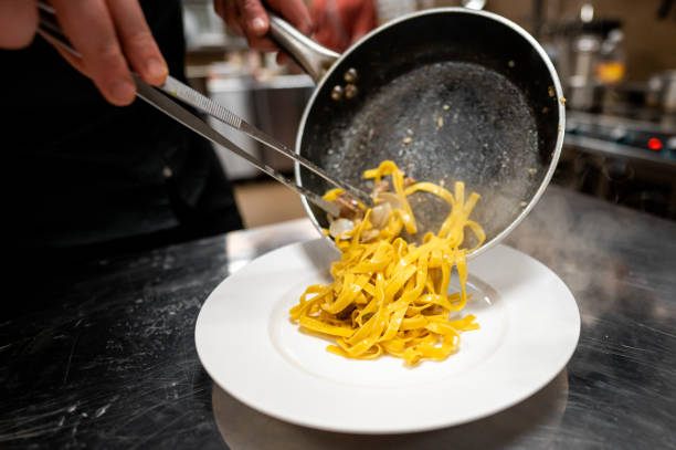 istock A chef in a professional kitchen serves freshly cooked pasta from a pan onto a plate using tongs. The scene captures the culinary process and the attention to detail in food presentation 2185878353