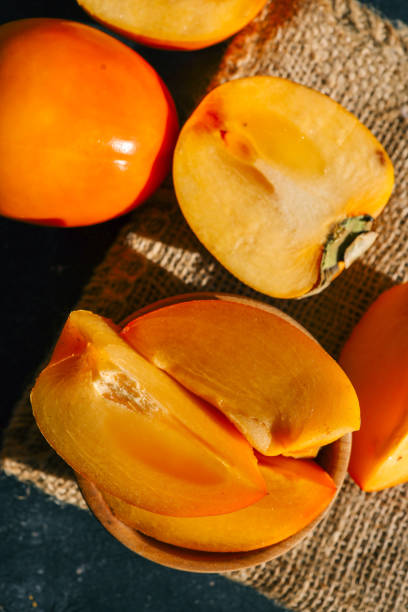 istock Sliced and whole persimmons arranged on a dark textured surface with natural light and burlap, showcasing vibrant colors and rustic simplicity. Perfect for food, seasonal, and healthy living themes 2185879641