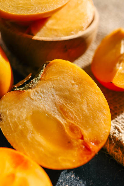 istock Sliced and whole persimmons arranged on a dark textured surface with natural light and burlap, showcasing vibrant colors and rustic simplicity. Perfect for food, seasonal, and healthy living themes 2185879648