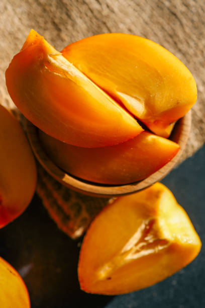 istock Sliced and whole persimmons arranged on a dark textured surface with natural light and burlap, showcasing vibrant colors and rustic simplicity. Perfect for food, seasonal, and healthy living themes 2185879650