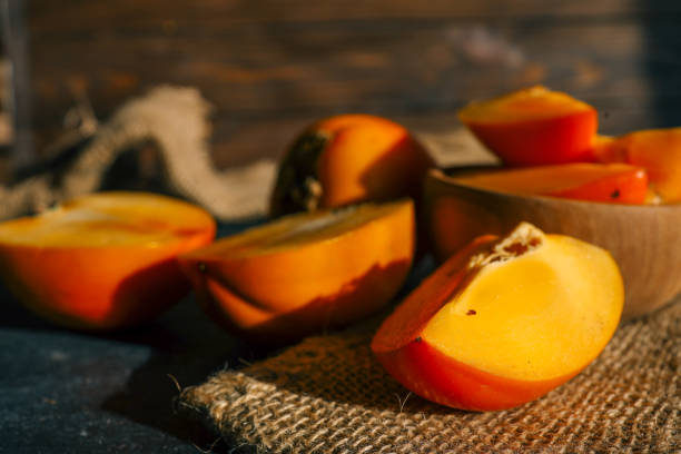 istock Sliced and whole persimmons arranged on a dark textured surface with natural light and burlap, showcasing vibrant colors and rustic simplicity. Perfect for food, seasonal, and healthy living themes 2185879654