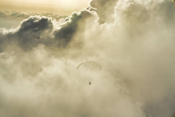 A paraglider flying through dense mist and illuminated clouds during sunset.