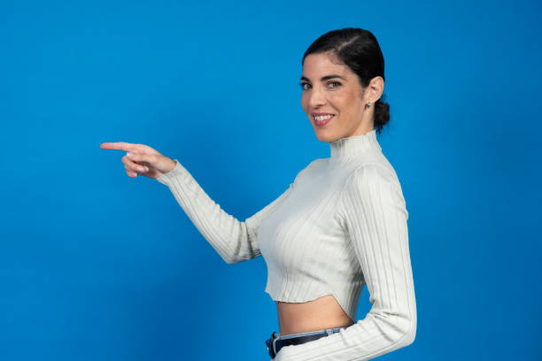 istock Smiling woman pointing finger showing something on blue background 2185881053