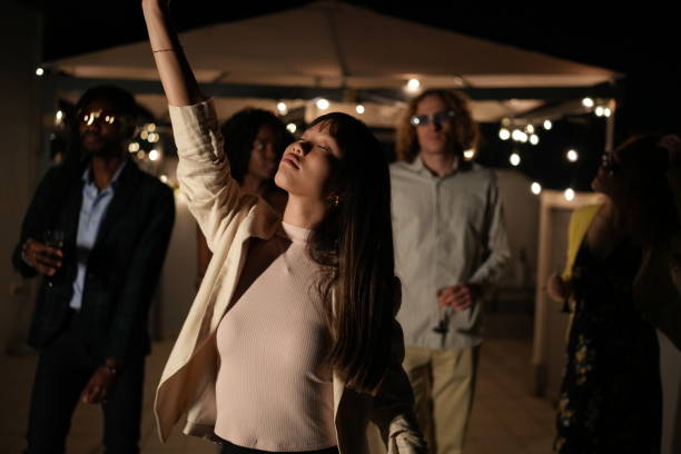 Young woman dancing with raised arm, enjoying a night party with multi-ethnic friends