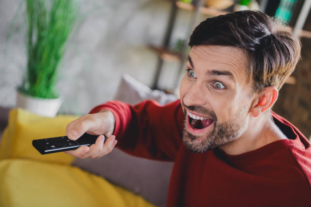 istock Enthusiastic young man enjoying his weekend indoors, immersed in a riveting show, wearing a cozy jumper in a stylish apartment. 2185883464