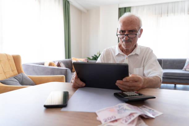 istock Senior man managing finances, holding cash and using calculator at home 2185884685