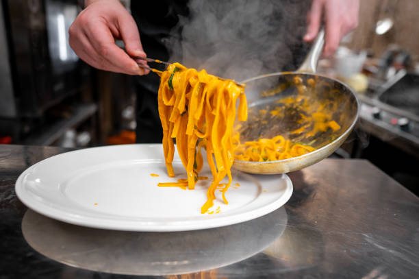 istock A chef serves steaming pasta onto a plate in a professional kitchen, showcasing culinary skills and delicious Italian cuisine. The scene captures the essence of gourmet cooking and fine dining. 2185885375