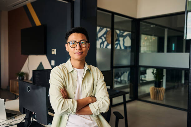 Young asian computer programmer sitting with crossed arms in modern office