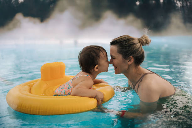 Loving moment between mother and toddler in a warm outdoor pool A tender moment of connection between a mother and her toddler as they touch noses and share a smile in a warm outdoor pool. The child sits in a yellow inflatable float, while steam rises from the water. pool gate stock pictures, royalty-free photos & images