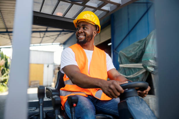 istock Cheerful black industry worker in working uniform driving forklift at industrial zone and looking away. 2185887094