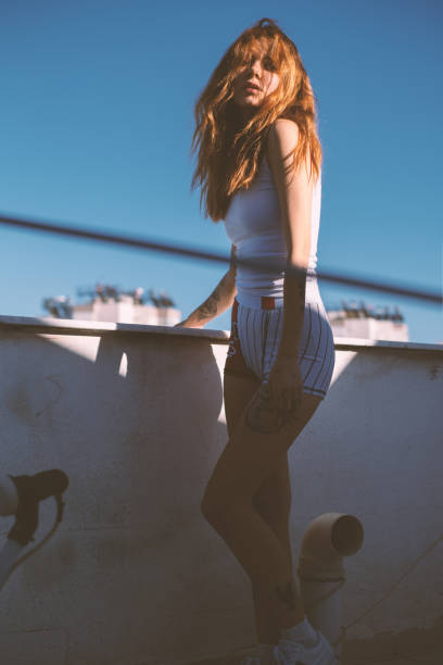 An attractive young woman posing on a rooftop under sunlight.