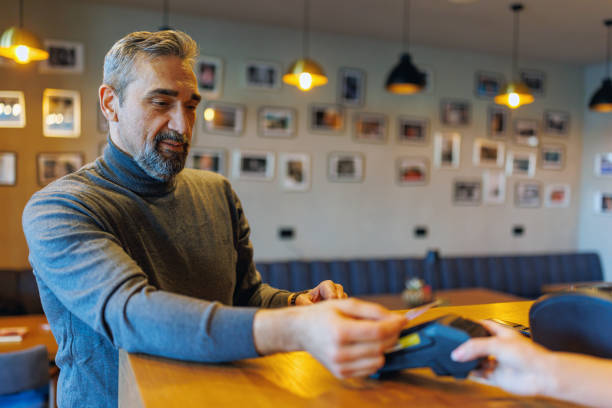 istock Man pays at counter using credit card, cafe atmosphere lively. 2185891530