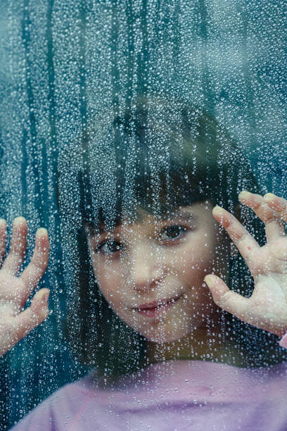 istock Little girl looking through window with rain drops 2185893785